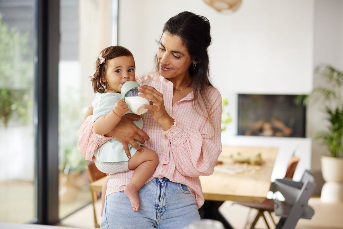 Mother holding a child drinking from a cup in a kitchen.
Ibu mendukung anak yang minum daripada cawan di dapur.